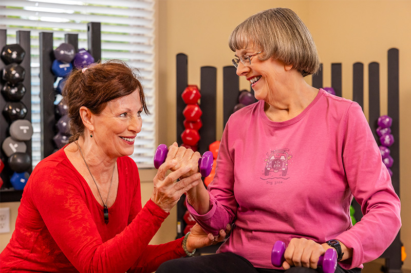 Senior woman working with a personal trainer lifting weights in a gym